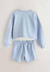 Šviesiai mėlynas medvilninis laisvalaikio drabužių komplektas, susidedantis iš trumpinto džemperio su ribinėmis rankogaliais ir atitinkančių šortų su elastiniu juosmeniu.