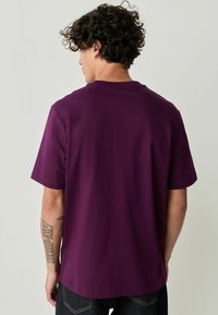 Paarse T-shirt met korte mouwen, gemaakt van zachte stof. Bevat een ronde hals en een rechte snit, met een gladde, effen textuur.