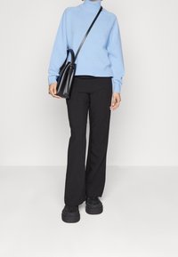 Pull col roulé bleu clair ; coupe décontractée. Pantalon noir évasé ; texture lisse. Sac à main noir au design structuré. Baskets noires épaisses.