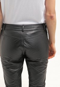 Černé kožené kalhoty s hladkým povrchem, s mírně zvýšeným pasem a zadními kapsami, zdobené viditelnými švy.