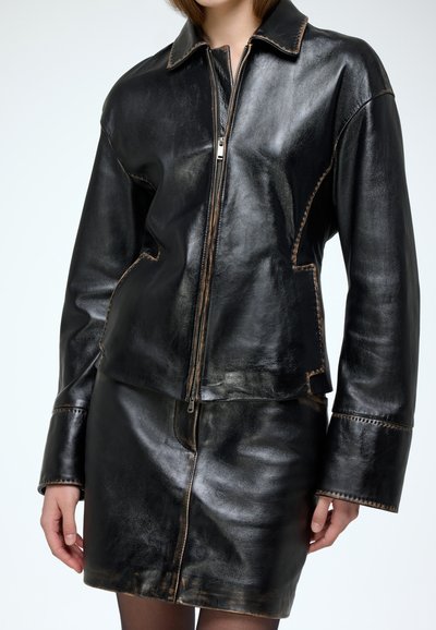 Black leather jacket with a zip closure, oversized collar, and contrasting stitching. Paired with a matching leather skirt.