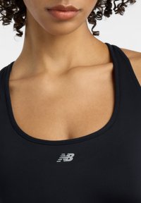 Débardeur de sport noir en tissu lisse, avec un décolleté en scoop et un petit logo gris sur la poitrine.