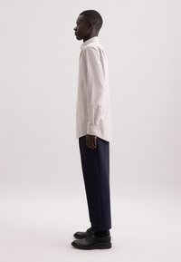Camicia a maniche lunghe da uomo in motivo a quadri chiari, con colletto a punta e polsini con bottone, abbinata a pantaloni blu scuro e scarpe nere.