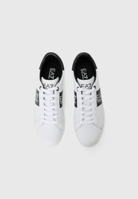Sneakers albe cu un finisaj din piele netedă, accente negre și o curea cu logo peste mijloc. Prezintă un design cu șireturi și vârf rotund.