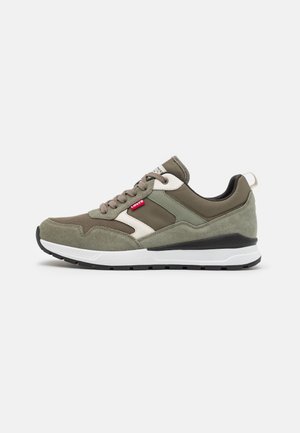 Baskets vert olive et beige avec des panneaux en suède et en mesh, des lacets marron, une semelle blanche, une semelle extérieure noire et une étiquette rouge Levi's sur le côté.