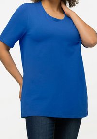 T-shirt bleu à manches courtes en coton doux. Présente un col rond et une coupe décontractée, contrastant avec un jean en denim foncé.
