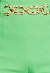 Tissu vert avec une texture lisse, mettant en avant une ceinture en chaîne dorée audacieuse avec des maillons ronds et des accents scintillants.