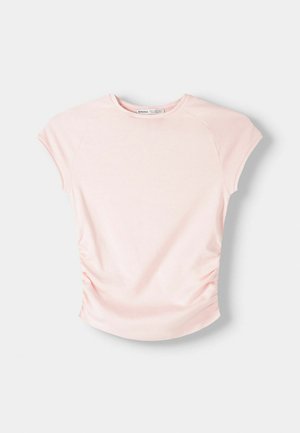 Haut rose clair à manches courtes avec un col rond. Présente des fronces sur les côtés et une texture douce et lisse. Le tissu semble extensible et léger.