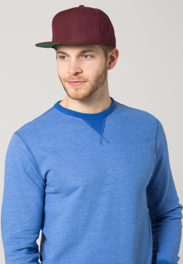 Burgundi snapback müts lame äärega, seljas sinine pika varrukaga särgiga, millel on ümar kaelus ja tekstuuriga kangas.
