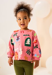 Roza pulover z prazničnimi vzorci, kot so drevesa, darila in snežaki; sproščen dizajn z dolgimi rokavi, kombiniran z zelenimi pajkicami.