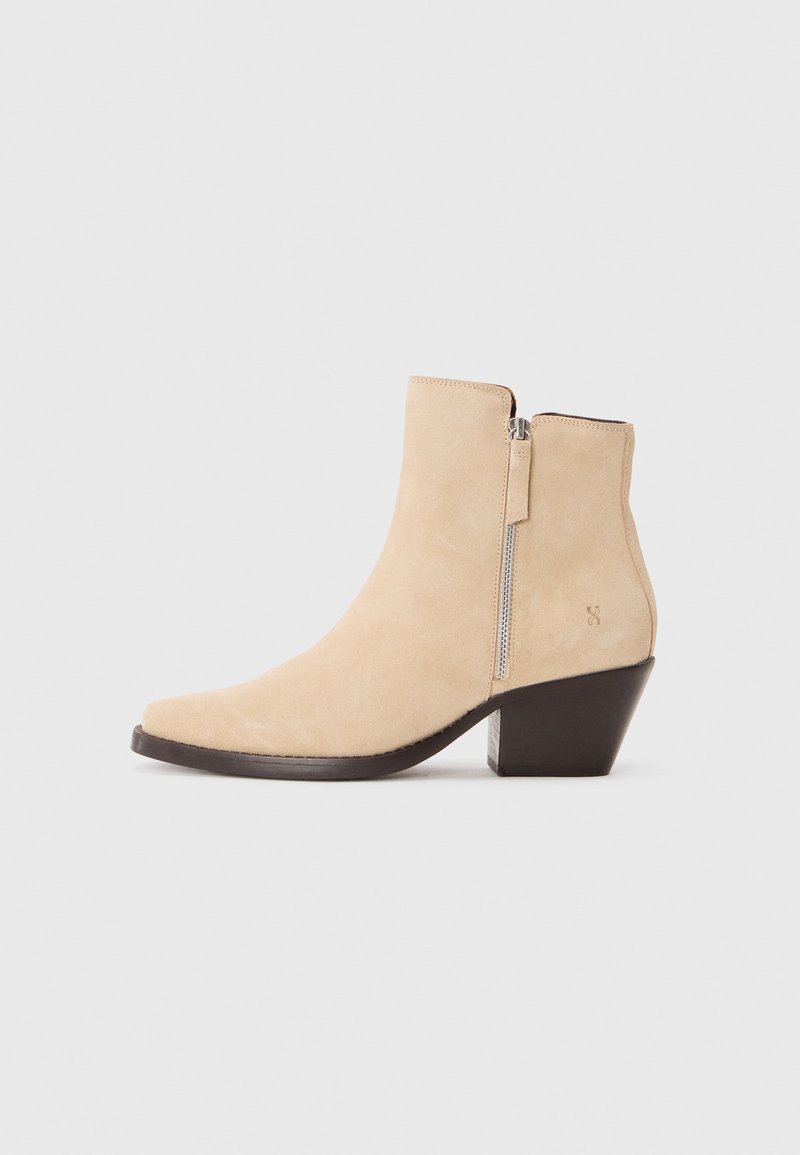 Stivale alla caviglia in suede beige con cerniera laterale e tacco stack nero, mostrato in profilo su uno sfondo bianco.