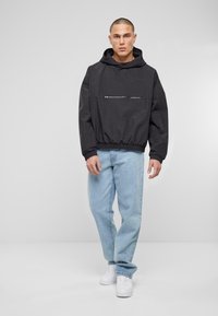 Felpa nera con cappuccio e tasca a zip frontale, polsini e orlo elasticizzati, abbinata a jeans blu chiaro e sneakers bianche.
