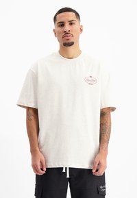 Lichtbeige oversized katoenen t-shirt met korte mouwen. Beschikt over een klein rood logo op de borst en een afgewerkte zoom. Soepele textuur, casual pasvorm.