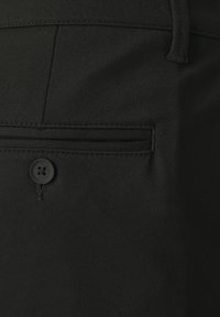 Pantalones de tela negra que cuentan con un bolsillo trasero con una abertura horizontal y cierre de botón redondo. Textura suave con detalles cosidos.