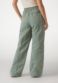 Pantaloni largi de culoare verde deschis, dintr-un material texturat. Au o talie elastică și un buzunar cu fermoar pe spate pentru un detaliu suplimentar.
