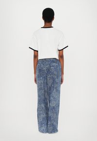 White t-shirt with black trim paired with loose-fitting, blue patterned denim pants. Visible back pockets on the pants.