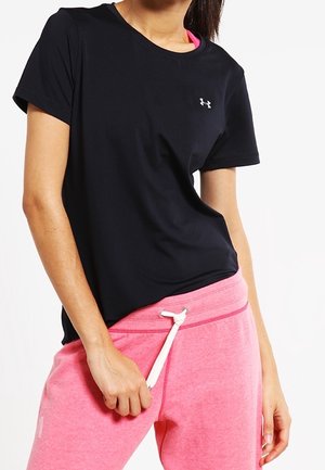 Kobieta ubrana w czarną, krótkorękawową koszulkę Under Armour i różowe spodnie dresowe, regulująca biały sznurek w talii.