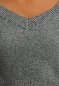 Szary sweter z dzianiny z dekoltem w kształcie litery V. Materiał ma miękką fakturę i subtelny melange. Widoczny prążkowany wzór na linii dekoltu.