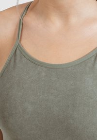 Top sin mangas verde oliva con tirantes finos y escote redondeado, hecho de una tela suave y elástica. Textura lisa y ajuste entallado.
