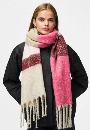 Rosa och krämfärgad scarf med fransar, med ett randigt mönster och ett mjukt, texturerat tyg. Bärs över en svart vadderad jacka.