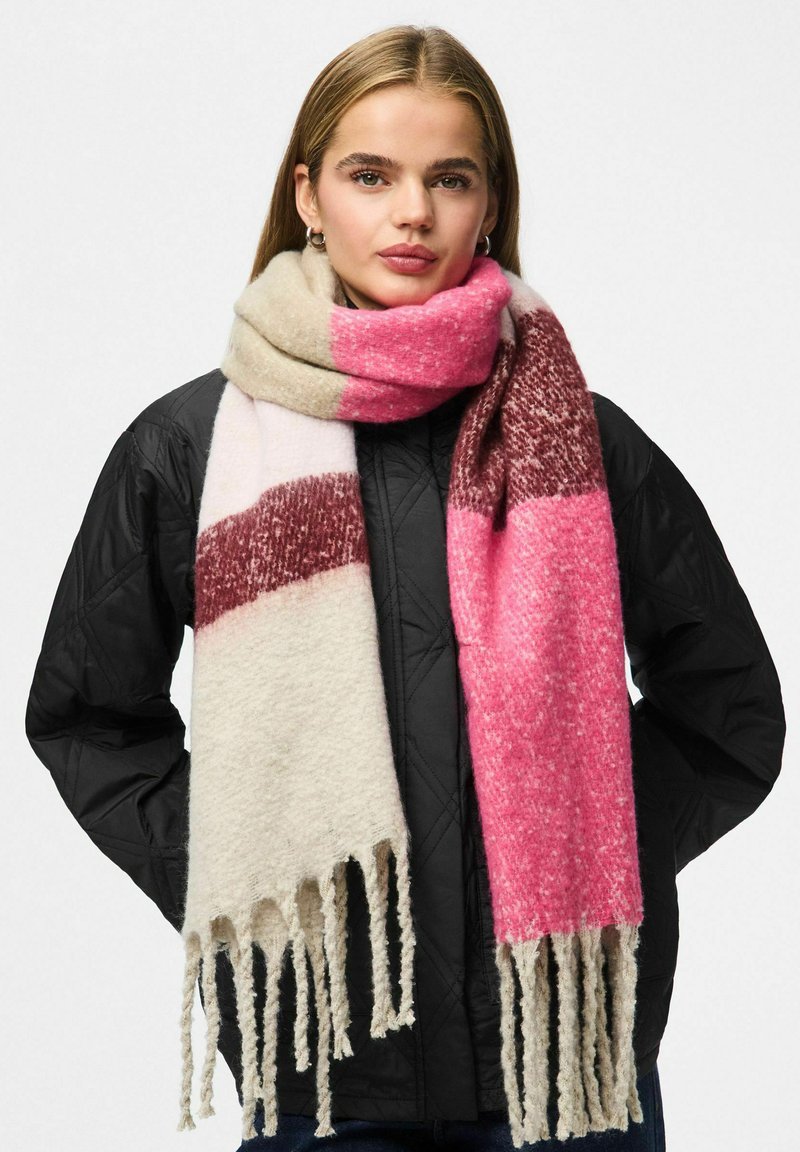 Bufanda rosa y crema con flecos, con un patrón a rayas y un tejido suave y texturizado. Usada sobre una chaqueta negra acolchada.