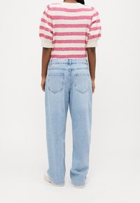 Suéter de rayas de manga corta en rosa y crema, combinado con unos vaqueros de talle alto en azul claro, de corte holgado y con dos bolsillos en la parte posterior.
