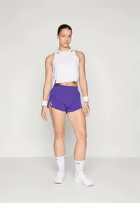 Beli skrajšani športni top, vijolične kratke hlače z logotipom Nike, bele zapestnice in športne nogavice. Preprost dizajn z modernim krojem in barvami.