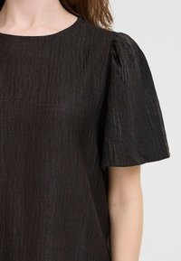 Top nero con texture, maniche a sbuffo corte. Presenta un colletto rotondo e sottili strisce verticali. Realizzato in tessuto leggero.