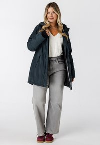 Donker teal ritsjack, textuurstof, oversized pasvorm, in combinatie met een crèmekleurige kabelgebreide sweater en lichtgrijze brede jeans, bordeaux sneakers.