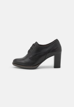 Chaussure Oxford pour femme en cuir noir avec laçage à l'avant et talon moyen épais, vue de profil sur fond blanc.