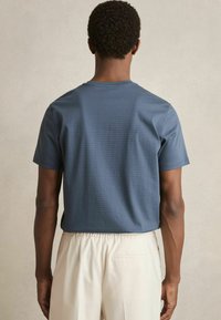 Tricou cu mânecă scurtă și gât rotund, de culoare albastru închis, cu o textură subtilă în dungi, asortat cu pantaloni bej deschis.