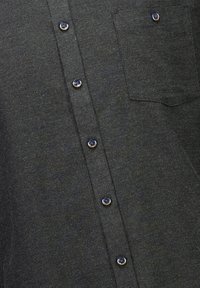 Camisa de botonadura en verde oscuro hecha de tejido texturizado, con botones negros con acentos dorados y un bolsillo en el pecho.