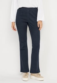 Navyblauwe stretch denim broek met een elastische tailleband, uitlopende pasvorm en een lichte textuur. Gecombineerd met beige sneakers.