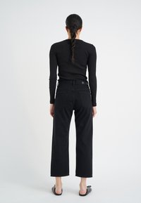 Svart ribbad långärmad topp i kombination med högmidjade vida svarta jeans med bakfickor och en slät textur. Svarta slip-on skor.