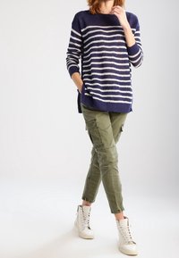 Marinblå och vitrandig stickad tröja med avslappnad passform, tillsammans med olivgröna cargobyxor och vita högskaftade sneakers.