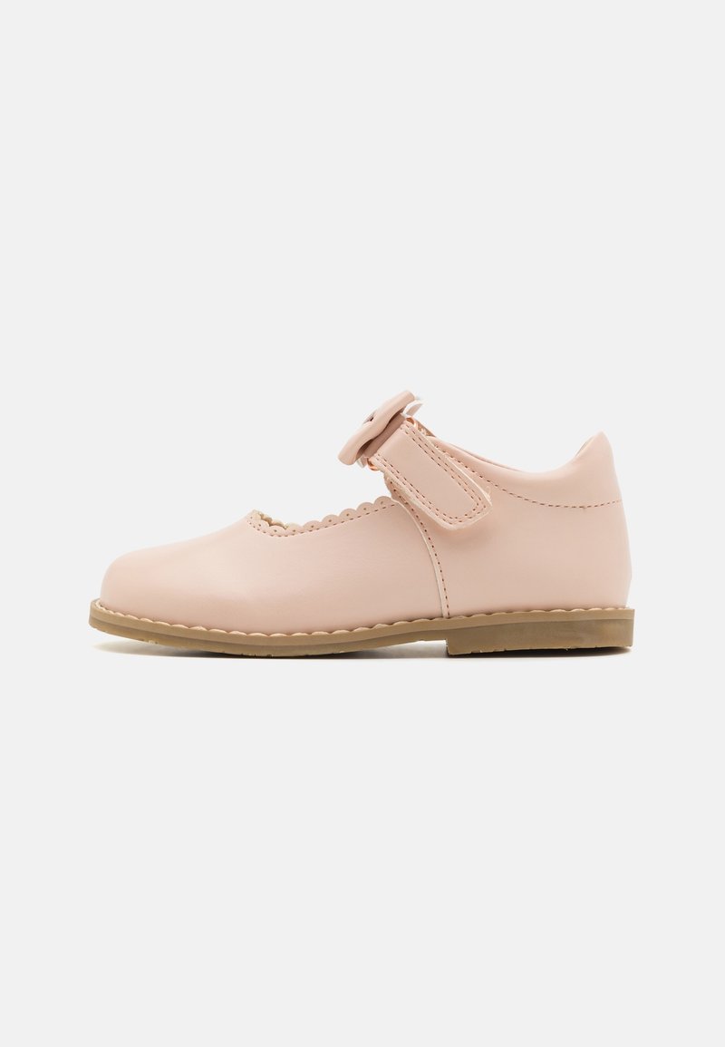 Zapato Mary Jane de cuero rosa con detalles ondulados, cierre de hebilla lateral y suela de goma plana. Textura suave y diseño de punta redondeada.