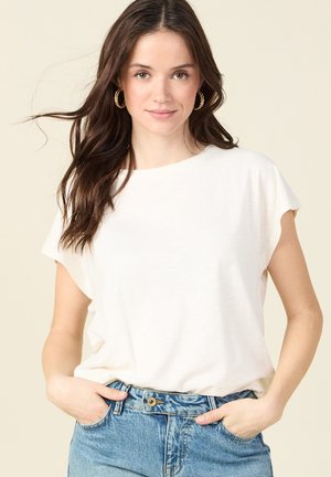 T-shirt beige chiaro con una vestibilità rilassata, scollo a girocollo e maniche corte arrotolate, abbinato a jeans in denim a vita alta.