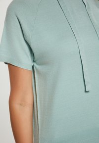 Hellblaue kurzärmlige Sweater mit einer lockeren Passform, ausgestattet mit einer Kapuze und strukturiertem Strickstoff. Nahtdetails sind an den Seiten sichtbar.