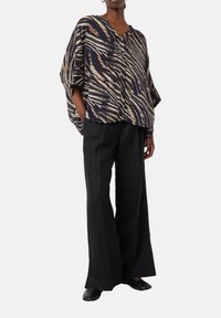 Blusa oversize a righe nere e beige con scollatura a V profonda e chiusura con bottoni. Abbinata a pantaloni neri a gamba larga e scarpe nere.