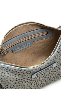 Interior de un bolso de cuero con estampado floral azul, con un forro beige, un bolsillo con cremallera, cremallera dorada y una etiqueta de marca.