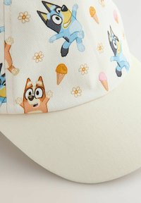 Casquette en tissu texturé, avec une base crème clair ornée d'un motif ludique de chiens de dessin animé, de fleurs et de cornets de glace.