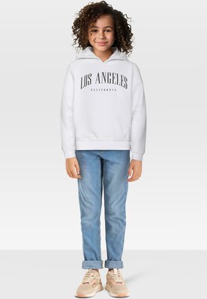 Hvit hettegenser med "LOS ANGELES" og "CALIFORNIA" trykket i svart, kombinert med lyseblå jeans og beige sneakers. Krøllete hår.