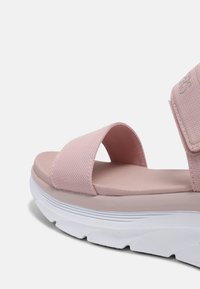 Sandalino rosa chiaro con una fascia superiore testurizzata, una soletta imbottita e una suola bianca e spessa con leggera curvatura e motivo a onda.