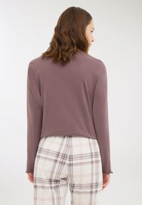 Długi rękaw, fioletowa bluzka wykonana z miękkiego materiału, z krótkim krojem i falbanastym wykończeniem, zestawiona z białymi spodniami w kratę z purpurowymi akcentami.