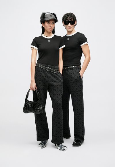 Μαύρα μπλουζάκια με λευκές λεπτομέρειες, εμπριμέ μαύρο παντελόνι, μαύρη τσάντα χειρός, γυαλιστερά ασημί παπούτσια και αξεσουάρ, όπως καπέλο και γυαλιά ηλίου.