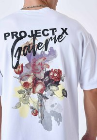 Witte t-shirt met korte mouwen met een bloemenpatroon in rood, roze en geel, met de tekst "PROJECT X Galerie" in zwart op de achterkant.