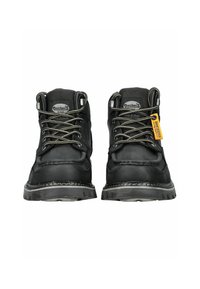 Bottes en cuir noir avec des œillets en métal, des lacets gris et une étiquette jaune. Le design présente une semelle robuste avec des coutures visibles et un col rembourré.