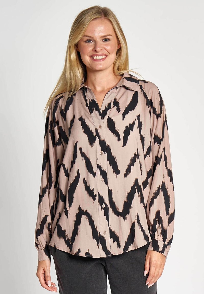 Long-sleeve blouse in a beige fabric with a black zigzag pattern. Features a classic collar and button-front closure. Soft texture.