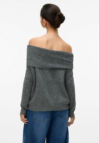 Grauer schulterfreier Pullover aus weichem Strickstoff, mit einem weiten gerippten Ausschnitt und langen Ärmeln. Kombiniert mit blauen Jeans.