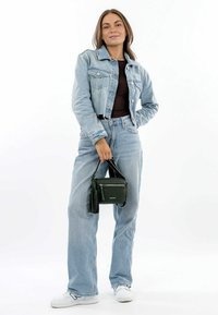 Giacca di jeans di colore azzurro chiaro, abbinata a jeans chiari a vita alta, sneakers bianche e una piccola borsa in pelle nera con frange.